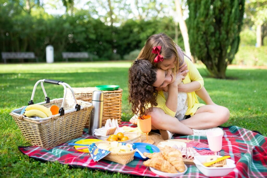 pexels-photo-7669136-7669136 A mother and daughter share a loving embrace on a picnic, surrounded by food and nature.