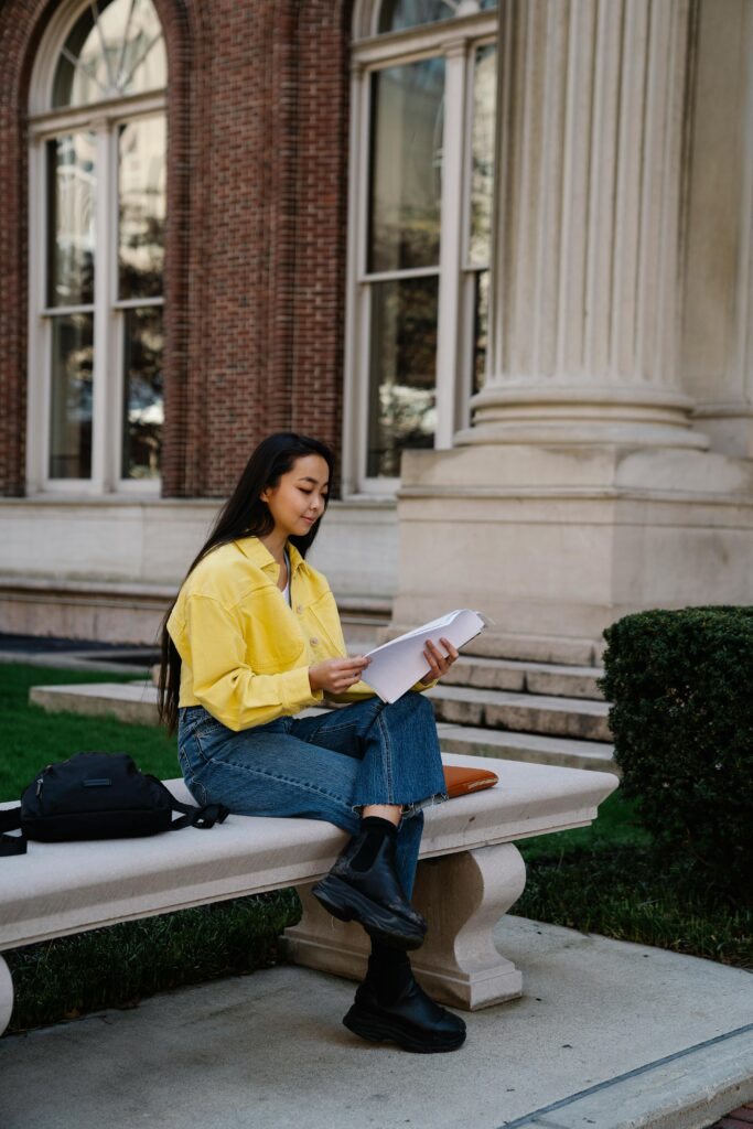 A young woman studying outdoors on a university campus bench, surrounded by classical architecture.